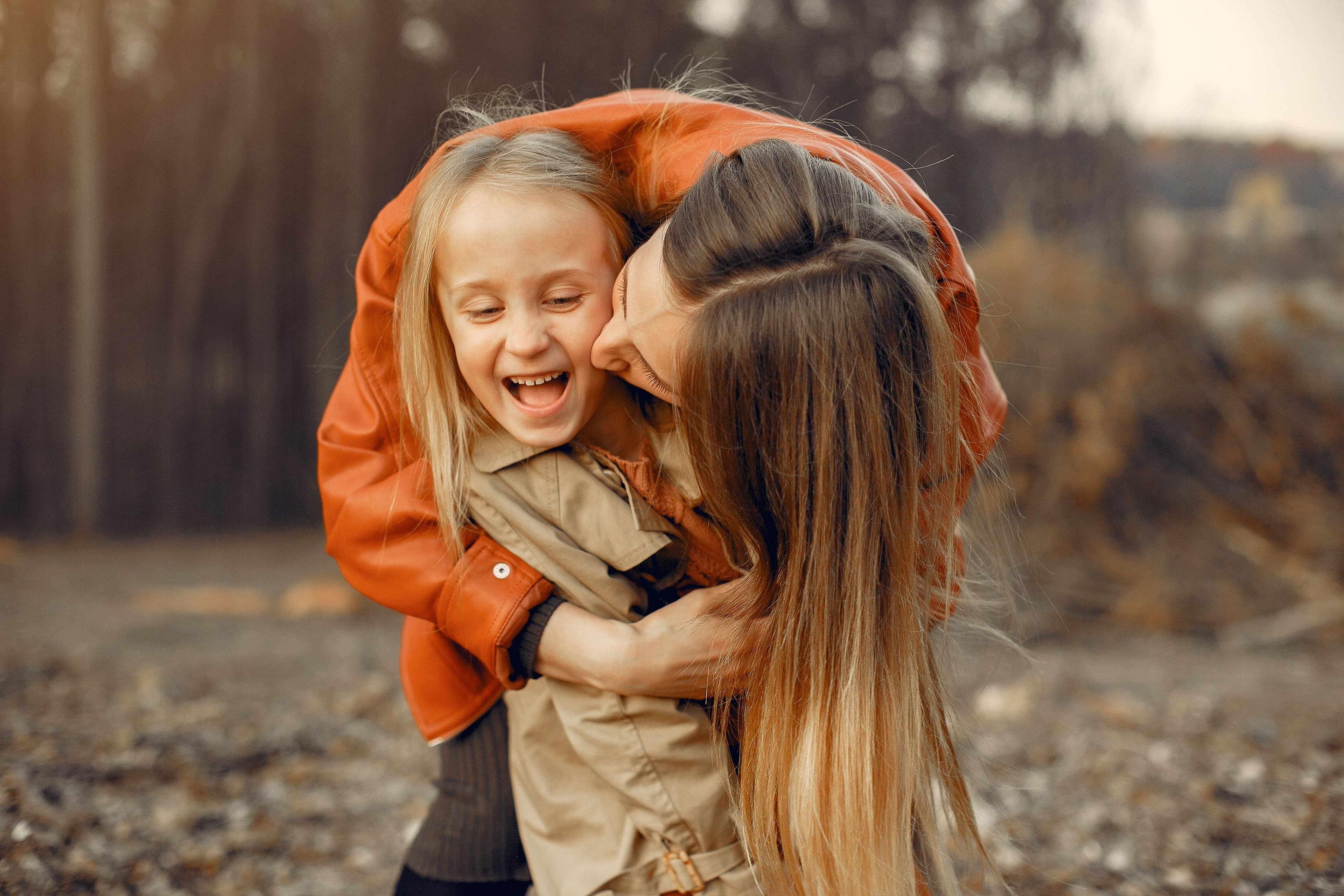 Mãe abraçando uma criança pequena sorridente, ao ar livre no outono